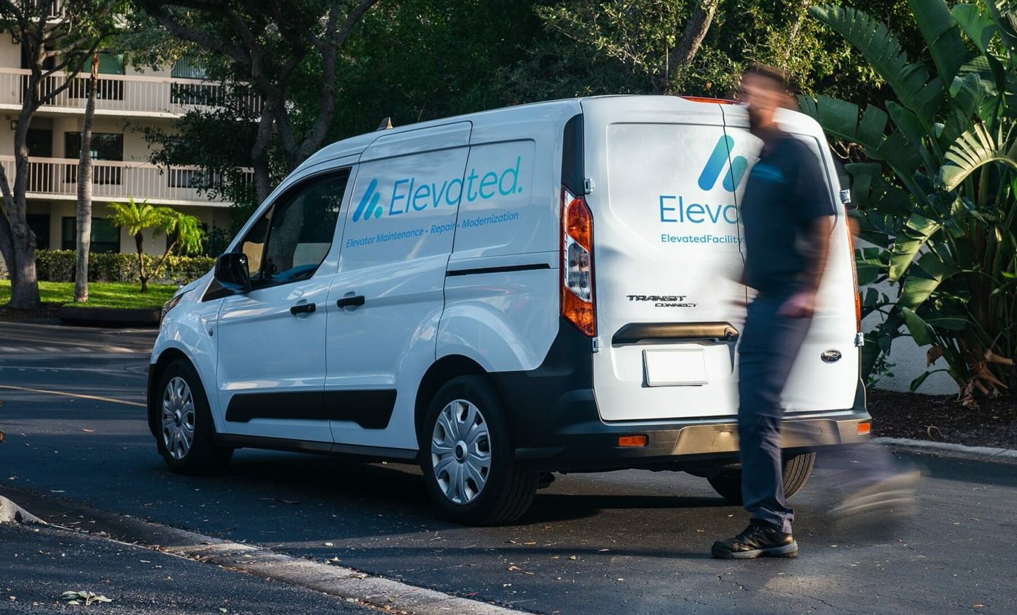 DSC08407-Edit-Edit-2-2 copy A white maintenance van with the logo of Elevated Facility Services parked outside a building with a technician walking past.