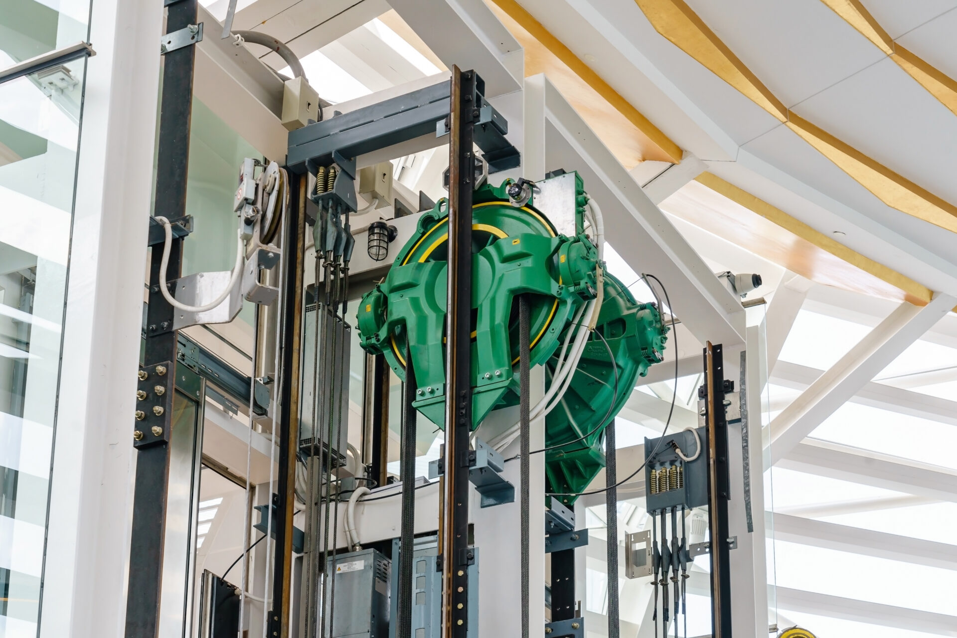 Modern elevator machinery with green gear mechanisms visible in a bright, architectural setting.