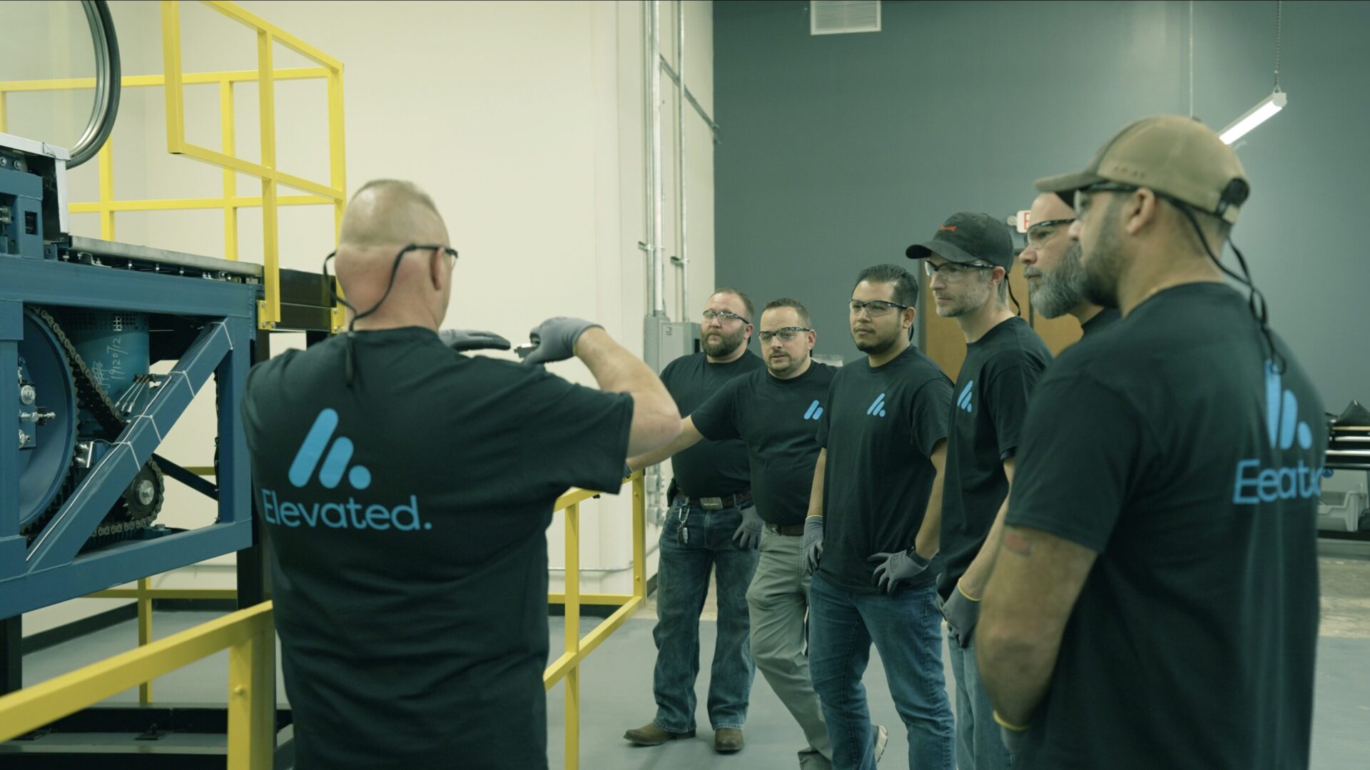 Group of elevator technicians in matching Elevated Facility Services shirts gather around a piece of machinery for hands-on training.