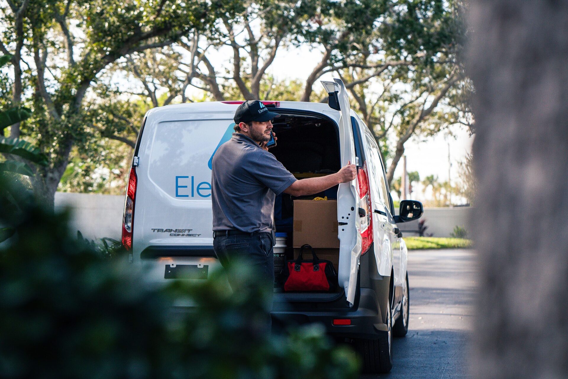 A technician standing at the back of a work van, unloading tools and equipment in a residential area.
